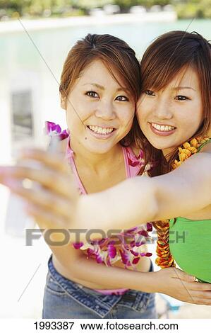 Stock Photo - Two Japanese Girls Take A Picture Of Themselves With A Camera Phone. Fotosearch
