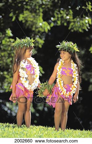 Stock Image - Two Keiki Hula Girls Hold Hands Face Each Other, Haku And Leis With Colorful Pareos. Fotosearch