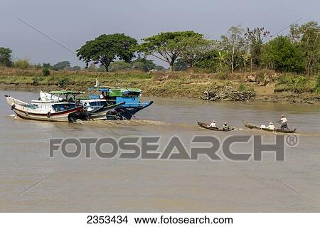 Picture - Two Long Tail Cargo Boats Pull A Small Canoe Upriver On The Yangon River; Yangon, Myanmar. Fotosearch