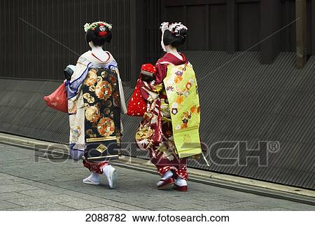 Stock Image - Two Maikos (Apprentice Geishas) Walking Away In A Street; Kyoto, Japan. Fotosearch