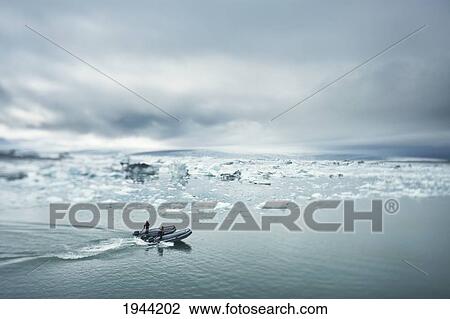 Stock Image - Two Men On A Nautical Vessel Driving Towards Chunks Of Ice In The Water; Jokulsarlon Iceland. Fotosearch