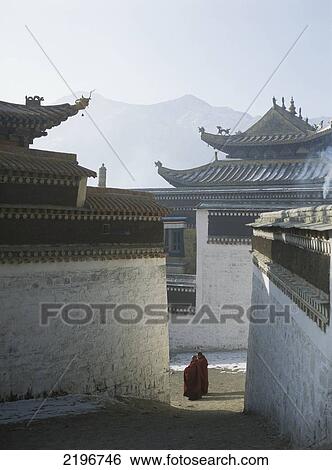 Stock Photograph - Two Monks Warming Themselves In The First Rays Of Sun, Tashikhyil Monastery, Labrang, Xiahe, Amdo, Eastern Tibet.. Fotosearch