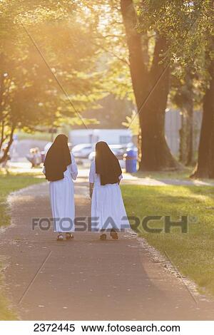 Stock Photography - Two Nuns Walk Together Down A Pathway Golden With Sunlight; Locarno, Ticino, Switzerland. Fotosearch
