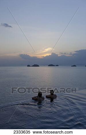 Stock Photography - Two People At The Edge Of An Infinity Pool Enjoying The Sunset; Ko Samui, Thailand. Fotosearch
