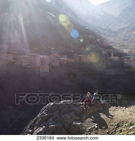 Picture - Two People Sit Eating On A Rock With Sunlight Streaming Over Them In The Valley Of The Atlas Mountains; Morocco. Fotosearch