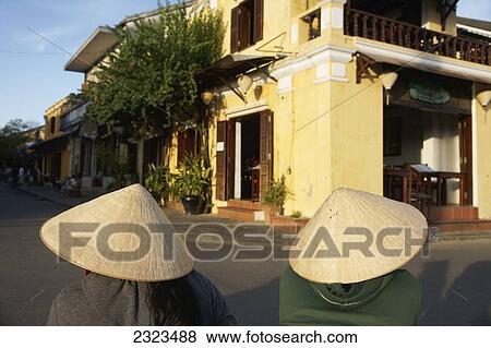 Stock Photo - Two People Wearing Conical Hats Sitting In Historic Town Of Hoi An; Vietnam. Fotosearch