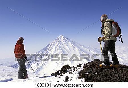 Stock Image - Two Skiers Admiring Snowy Peak. Fotosearch