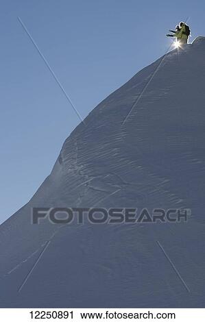 Stock Image - Two snowboarders stand at the top of a snow covered steep mountain slope; Austria. Fotosearch