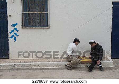 Two teenage boys play a board game sitting on the pavement outside their home in the Jewish town of Erriadh; Erriadh, Djerba, Tunisia View Large Photo Image Stock Photo - Two teenage boys play a board game sitting on the pavement outside their home in the Jewish town of Erriadh; Erriadh, Djerba, Tunisia. Fotosearch