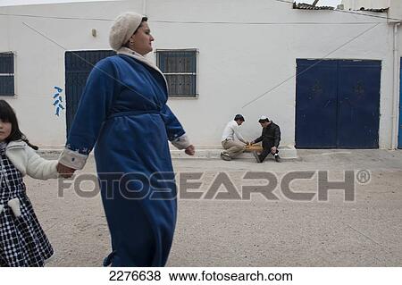 Stock Photo - Two teenage boys play a board game sitting on the pavement outside their home in the Jewish town of Erriadh, formally known as Hara Seghira ( the 'Little Ghetto' ). Djerba. Tunisia. North Africa.. Fotosearch
