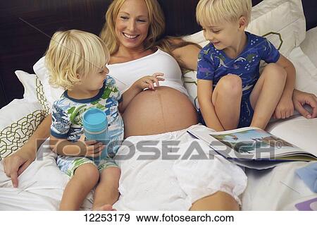 Two toddlers study their mother's pregnant belly while she reads to them in bed; Santa Barbara, California, United States of America View Large Photo Image Stock Photo - Two toddlers study their mother's pregnant belly while she reads to them in bed; Santa Barbara, California, United States of America. Fotosearch