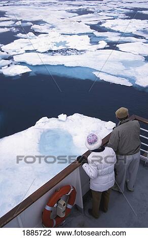 Stock Image - Two Tourists Looking Over Boat Railing At Floating Ice. Fotosearch