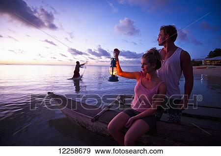 Stock Photo - Two tourists sitting at the water's edge at sunset; Savaii Island, Samoa. Fotosearch