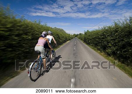 Two Women Cycling On Tandem Down Road In The Countryside; Kent England View Large Photo Image Stock Image - Two Women Cycling On Tandem Down Road In The Countryside; Kent England. Fotosearch