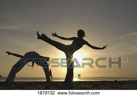Stock Image - Two Women Silhouetted Doing Capoeira On Beach At Sunset. Fotosearch