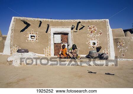 Stock Image - Two Women Siting In Front Of Decorated Mud Hut, Jaisalmer, Rajasthan, India. Fotosearch