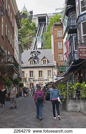 Stock Photo - Two women walk up cobblestone streets past shops toward a funicular as car ascends; quebec city quebec canada. Fotosearch