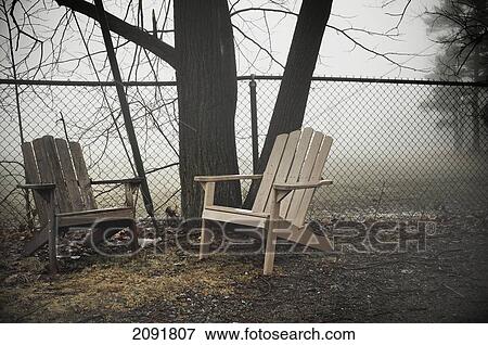 Two Wooden Adirondack Chairs By A Steel Fence On A Foggy Day; Otterburn Park, Quebec, Canada View Large Photo Image Stock Photo - Two Wooden Adirondack Chairs By A Steel Fence On A Foggy Day; Otterburn Park, Quebec, Canada. Fotosearch