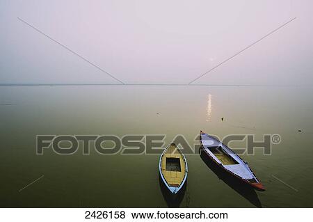 Stock Photo - Two wooden boats sit on the tranquil water of the Ganges; Varanasi, India. Fotosearch