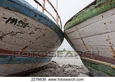 Two worn and weathered wooden boats on the shore with a fisherman mending his nets along the beach; Houmt Souk, Djerba, Tunisia View Large Photo Image Stock Photograph - Two worn and weathered wooden boats on the shore with a fisherman mending his nets along the beach; Houmt Souk, Djerba, Tunisia. Fotosearch