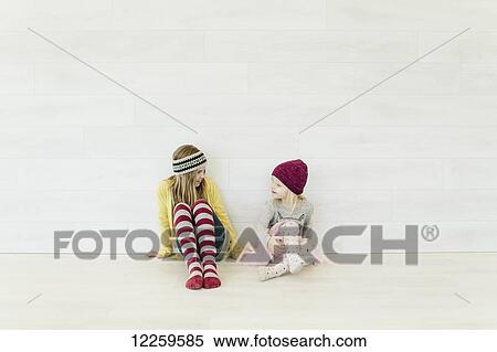 Stock Photography - Two young girls sit and talk against a white wall. Fotosearch