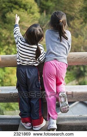 Two young girls standing together on rail fence pointing upwards; Kyoto, Japan View Large Photo Image Stock Photo - Two young girls standing together on rail fence pointing upwards; Kyoto, Japan. Fotosearch
