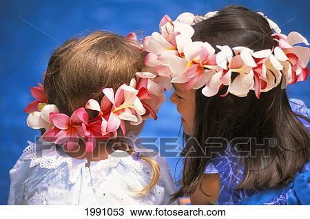 Stock Image - Two Young Girls With Plumeria Haku Leis Shot From Behind. Blue Background. Fotosearch