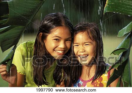 Stock Image - Two Young Hapa Girls Hide Under Banana Leaf Under Banana Leaf. Fotosearch