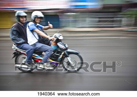 Picture - Two Young Men Ride A Motorbike Down A Road; Palembang Sumatra Indonesia. Fotosearch