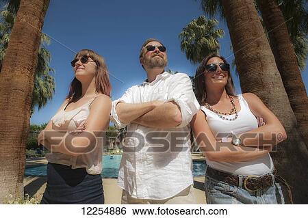 Stock Photograph - Two young women and a man standing by palm trees; Palm Springs, California, United States of America. Fotosearch