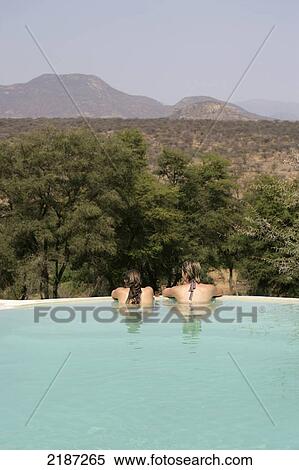 Stock Photography - Two young women in a swimming pool with a view of the Kenyan landscape; Sasaab, Kenya. Fotosearch