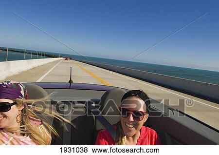 Two young women in the back of an open top sports car are being driven along Highway 1., Florida Keys. View Large Photo Image Stock Photo - Two young women in the back of an open top sports car are being driven along Highway 1., Florida Keys.. Fotosearch