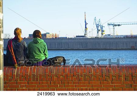 Two young women sit on a bridge ledge overlooking the river; Hamburg, Germany View Large Photo Image Stock Image - Two young women sit on a bridge ledge overlooking the river; Hamburg, Germany. Fotosearch