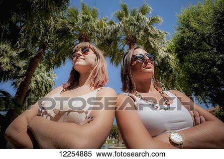 Stock Photography - Two young women standing by palm trees; Palm Springs, California, United States of America. Fotosearch