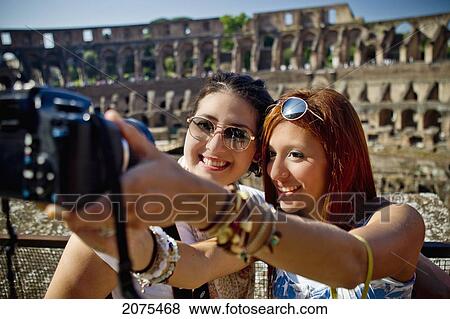 Stock Photo - Two Young Women Take A Picture Of Themselves With A Camera And The Colosseum In The Background; Rome Italy. Fotosearch