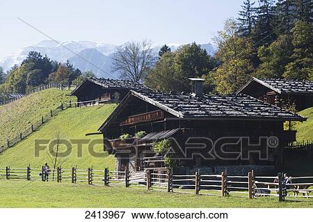 Stock Photo - Tyrolean style farm houses with green meadows and mountains and blue sky in the background; Kramsach, Austria. Fotosearch