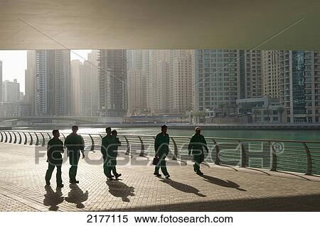 Stock Photography - UAE, Construction workers walking under bridge in Dubai Marina; Dubai. Fotosearch