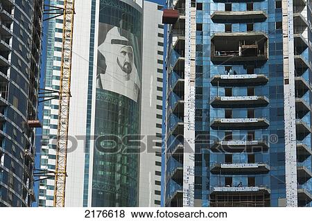 Stock Photo - UAE, Large portrait of Sheikh Mohammed Bin Rashid Al Maktoum on building beside other buildings under construction; Dubai. Fotosearch