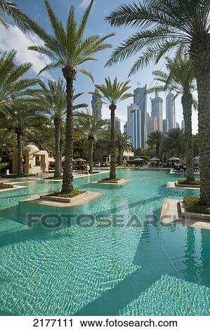 Stock Image - UAE, Swimming pool of One and Only Royal Mirage with tower blocks behind; Dubai. Fotosearch