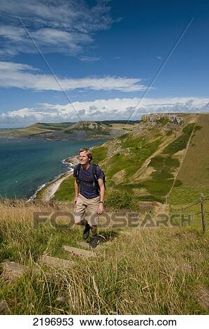 Stock Image - UK, Dorset, Walker going up stairs up to St Aldhelm's Head on South West Coastal Path; Purbeck. Fotosearch