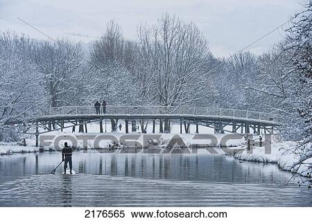 Stock Photography - UK, East Sussex, Man paddle boarding down River Ouse in snowy conditions; Lewes. Fotosearch