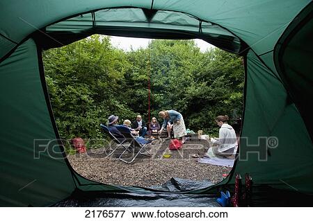 Stock Photo - UK, East Sussex, View out of tent to people beside campfire at Blackberry Wood campsite; Plumpton. Fotosearch