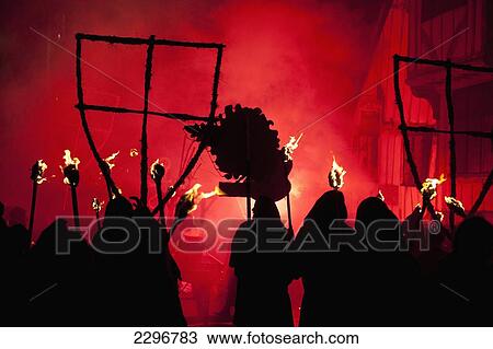 Stock Image - UK, England, East Sussex, Bonfire night; Lewes, Silhouettes of monks from Southover Bonfire Society lit by red flares on United Grand Procession down High Street. Fotosearch
