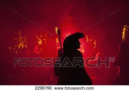 Stock Image - UK, England, East Sussex, Bonfire night; Lewes, Silhouette of pirate with burning torch from Southover Bonfire Society lit by red flares on United Grand Procession down High Street. Fotosearch