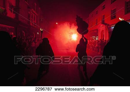 Stock Photo - UK, England, East Sussex, Bonfire night; Lewes, Silhouettes of monks from Southover Bonfire Society lit by red flares on United Grand Procession down High Street. Fotosearch