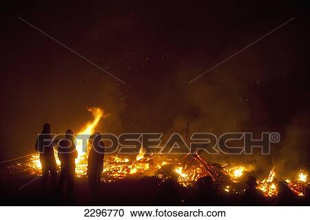 Stock Image - UK, England, East Sussex, People in front of remains of large bonfire at Newick Bonfire Night; Newick. Fotosearch