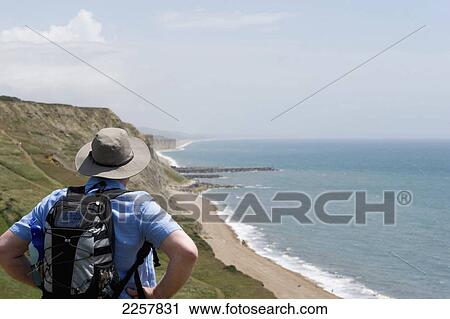 Stock Image - Uk, England, Rear View Of Man Looking At Jurassic Coast; West Dorset. Fotosearch