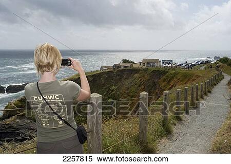 Stock Photography - Uk, England, Rear View Of Woman Photographing At Lizard Point; Cornwall. Fotosearch
