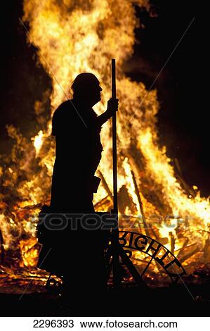 Stock Image - UK, England, Silhouette of man with banner in front of large bonfire at Battle Bonfire night; East Sussex. Fotosearch