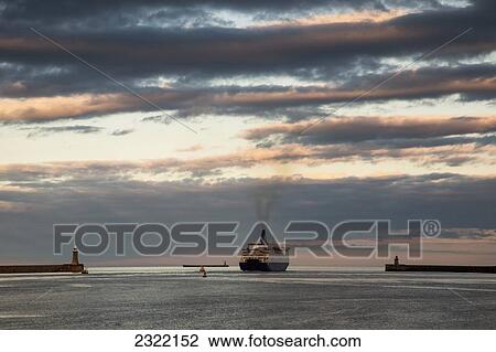 Stock Image - UK, England, Tyne and Wear, South Shields, Ship pulling into port at sunset. Fotosearch